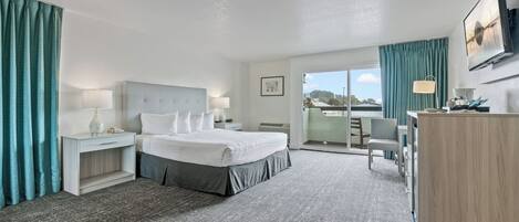 A hotel room with a bed, bedside tables, a desk, a chair, and a large window.