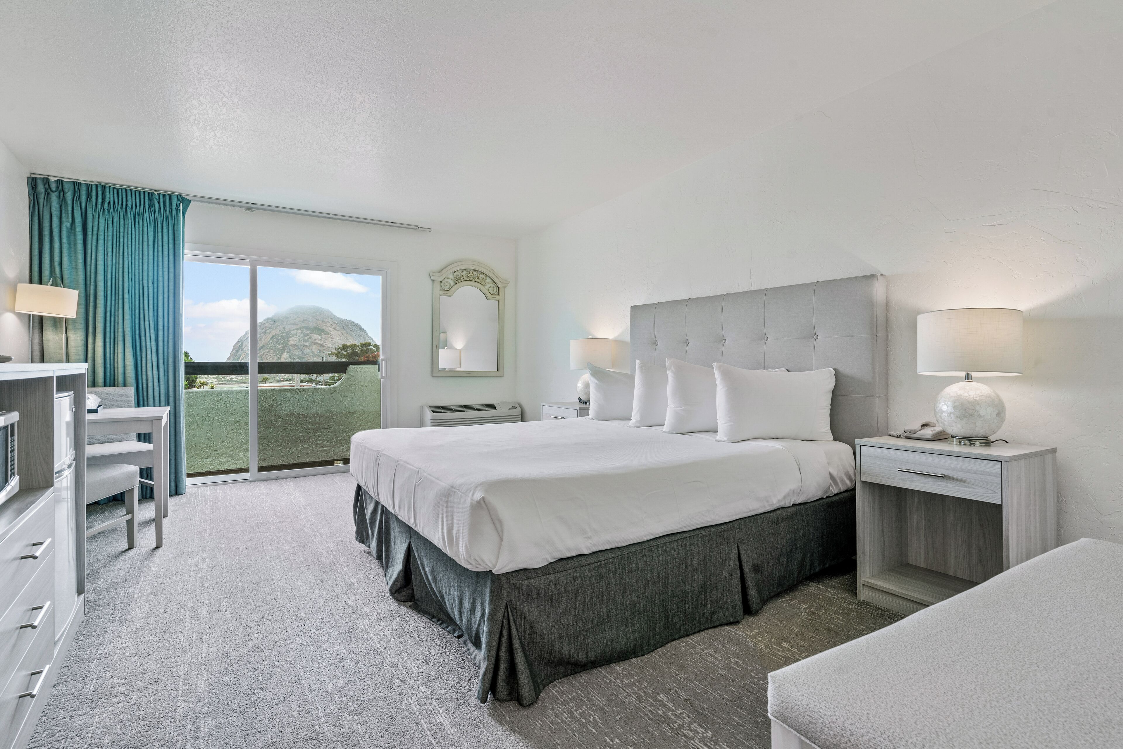 A hotel room with a large bed, a desk, and a chair. There is a view of a mountain through the window.
