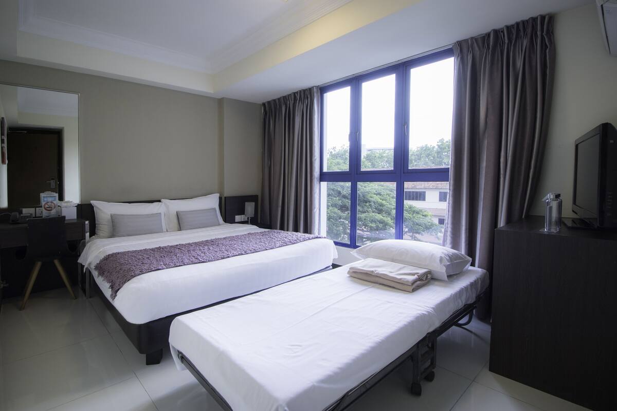 Habitación de hotel con dos camas, un escritorio, una silla, un televisor y una ventana con cortinas.