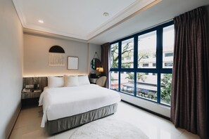 A modern bedroom with a large bed, a nightstand, a lamp, and a view of the outside. - Harbour Ville Hotel (Singapore)