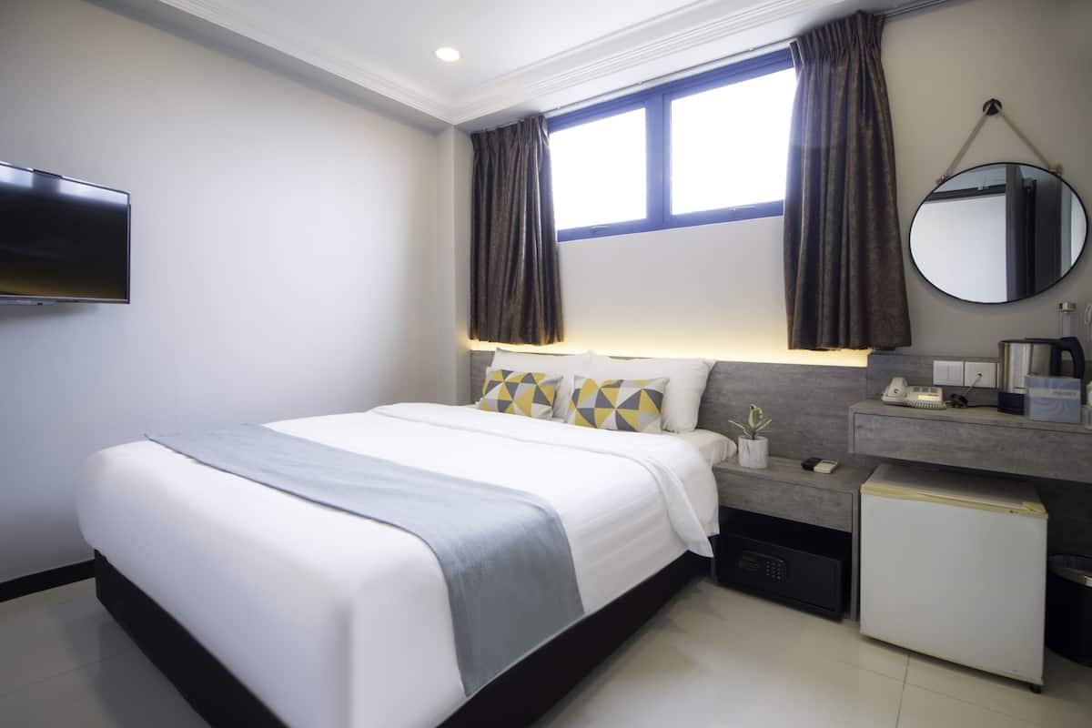 Una habitación de hotel moderna con una cama grande, un televisor de pantalla plana, un escritorio con teléfono y un refrigerador pequeño.