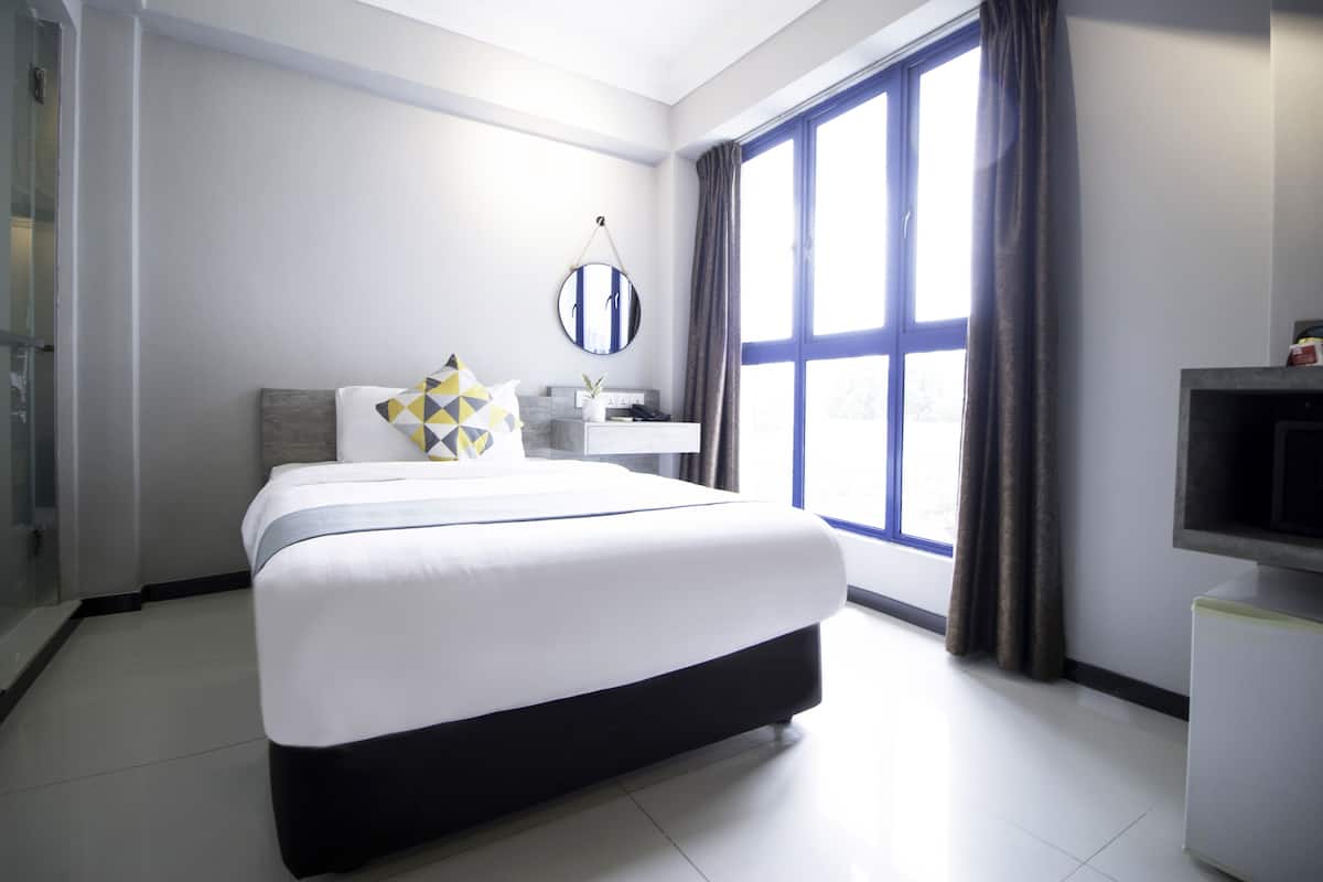 Una habitación de hotel moderna con una cama grande, una mesita de noche, un espejo y un televisor.