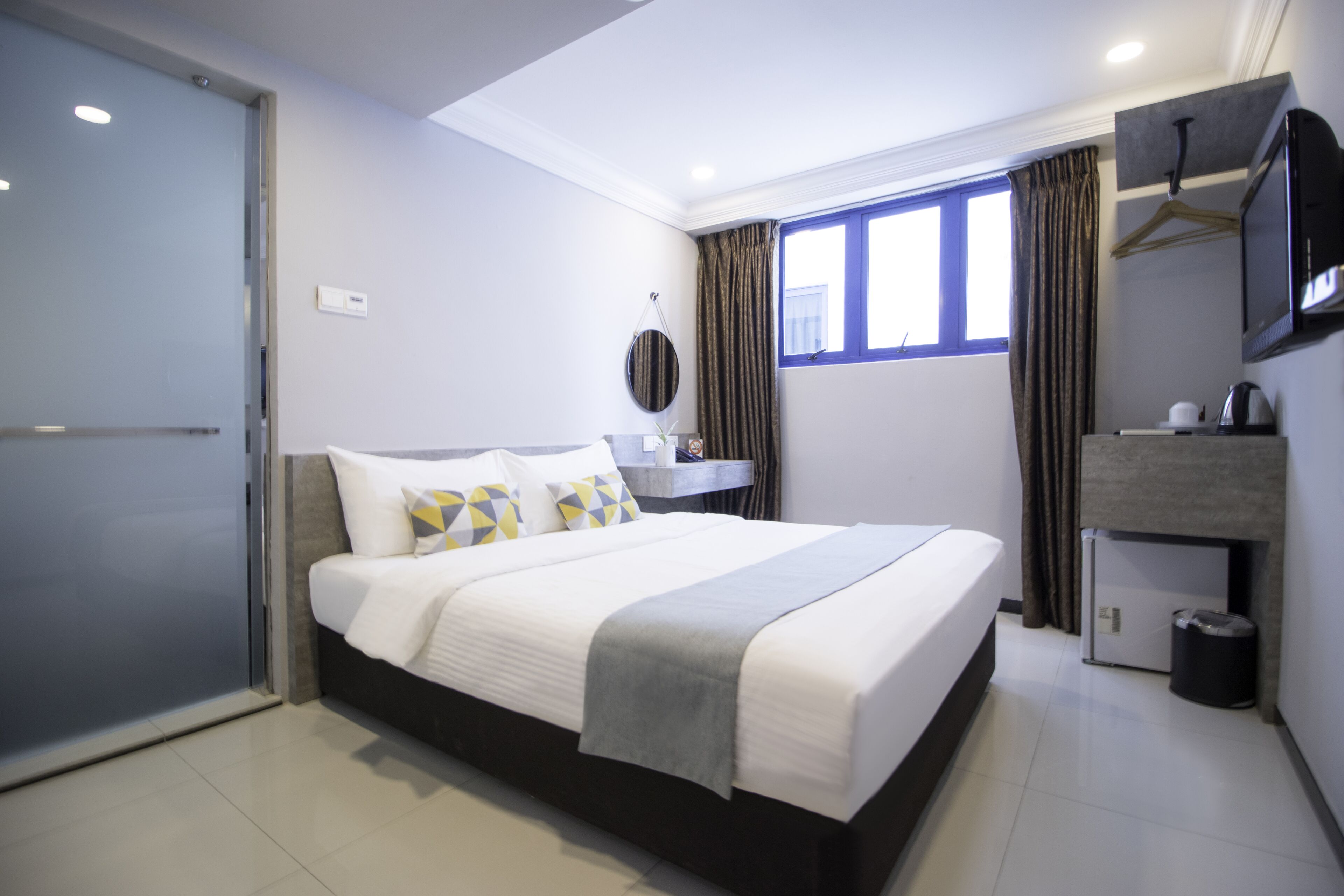 Una habitación de hotel moderna con una cama grande, un escritorio pequeño, un espejo y un televisor.