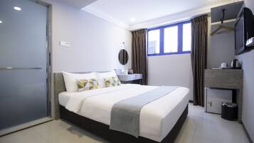 Una habitación de hotel moderna con una cama grande, un escritorio pequeño, un espejo y un televisor.