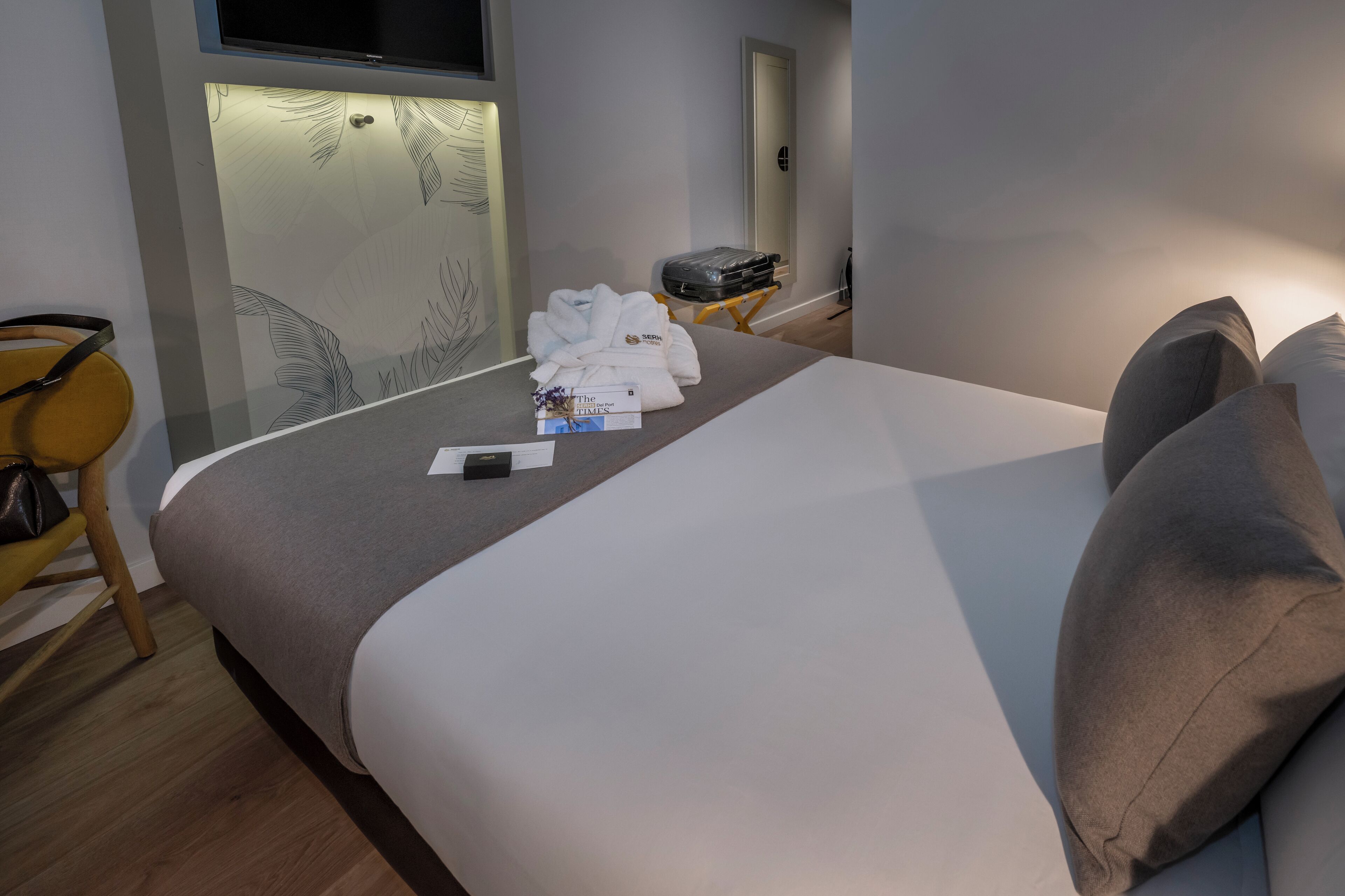 Una habitación de hotel con una cama, una mesita de noche con lámpara, una silla y una maleta.