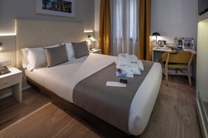 Una habitación de hotel con una cama grande, un escritorio, una silla y una mesita de noche con teléfono y lámpara.