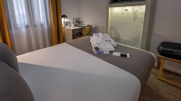 A hotel room with a bed, a desk, a chair, a TV, and a wall with a leaf pattern.