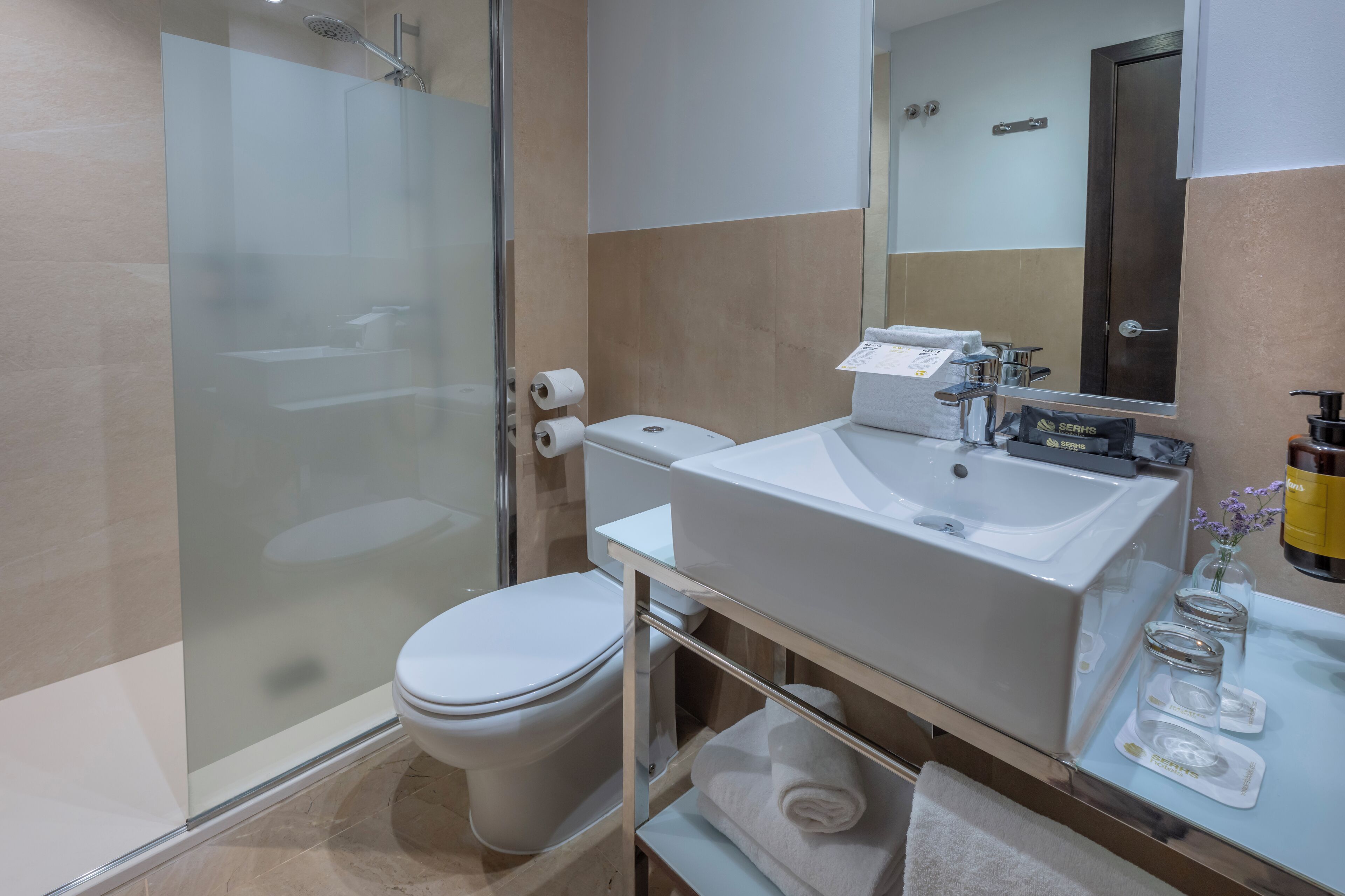 Un baño moderno con ducha de vidrio, inodoro blanco, lavamanos grande y un espejo.