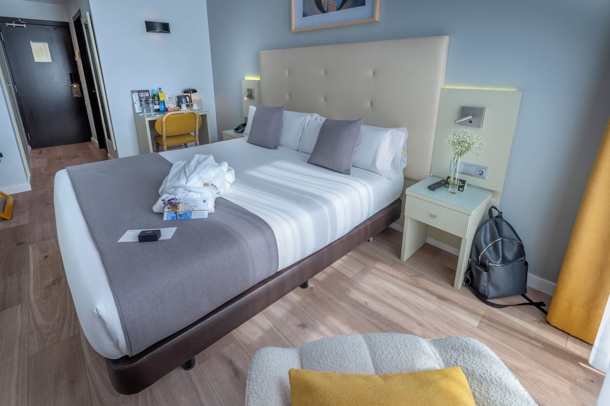 A hotel room with a large bed, a desk with a chair, a nightstand, and a suitcase.