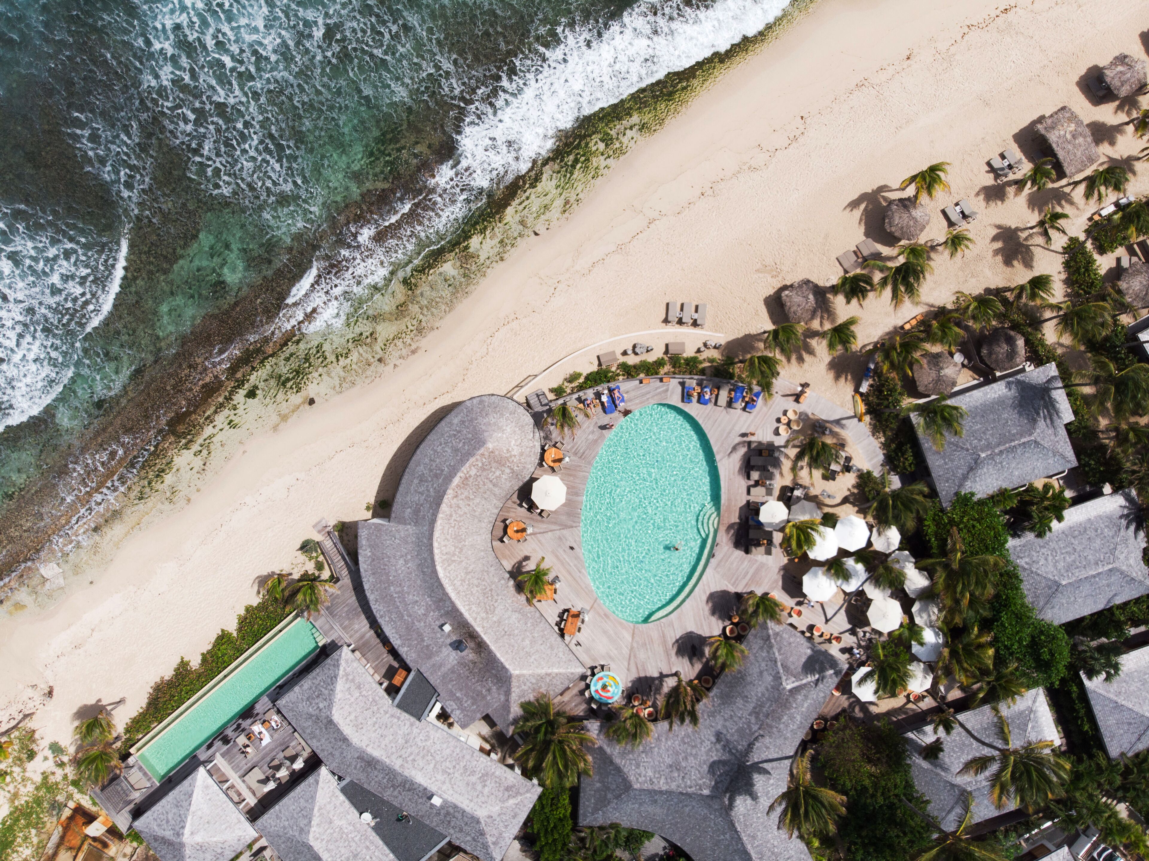 Vue aérienne d’un complexe hôtelier avec une piscine, une plage et des palmiers.
