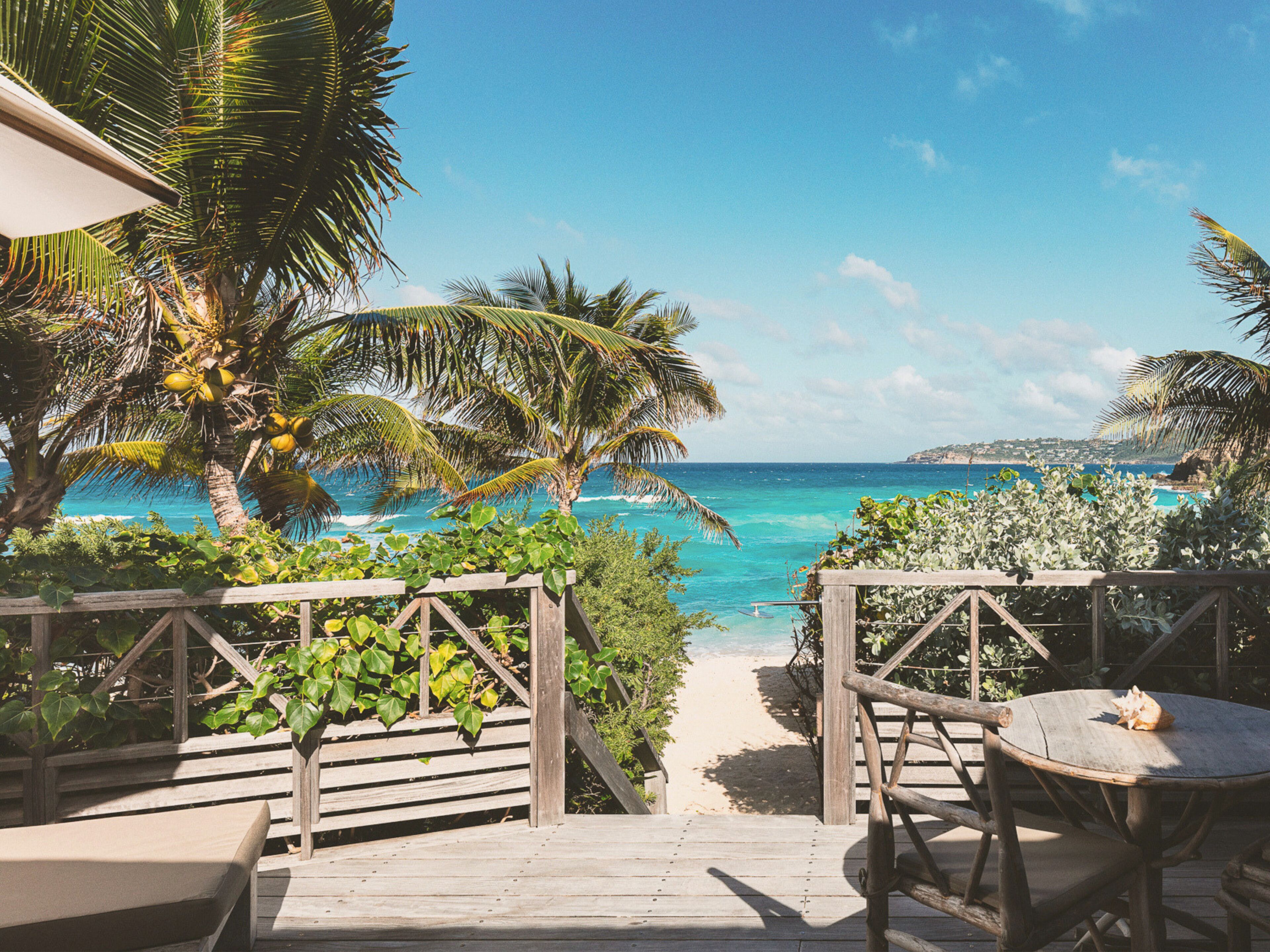 Une terrasse en bois qui mène à une plage bordée de palmiers et offrant une vue sur l’océan.
