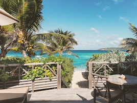 A wooden deck leading to a beach with palm trees and a view of the ocean.