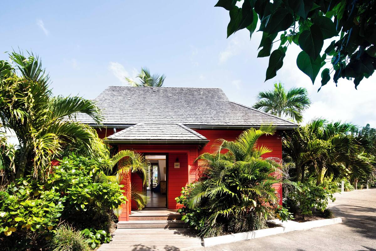 Un edificio rojo con techo gris, rodeado de abundante vegetación y palmeras.