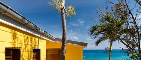 A yellow building with a wooden deck, a palm tree, and a view of the ocean.