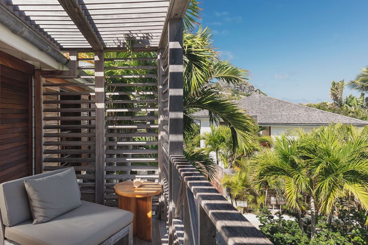 Un balcon agrémenté d’une pergola en bois, d’un coin salon avec des coussins et d’une petite table ronde.