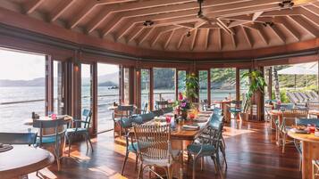 Un comedor amplio con suelo de madera y ventanas grandes con vistas a un cuerpo de agua.