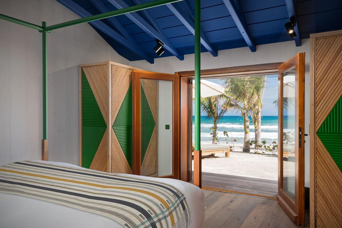 Une chambre avec un lit, une vue sur la plage et une porte donnant sur l’extérieur.