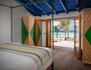 Un dormitorio con cama, vistas a la playa y una puerta que da al exterior.