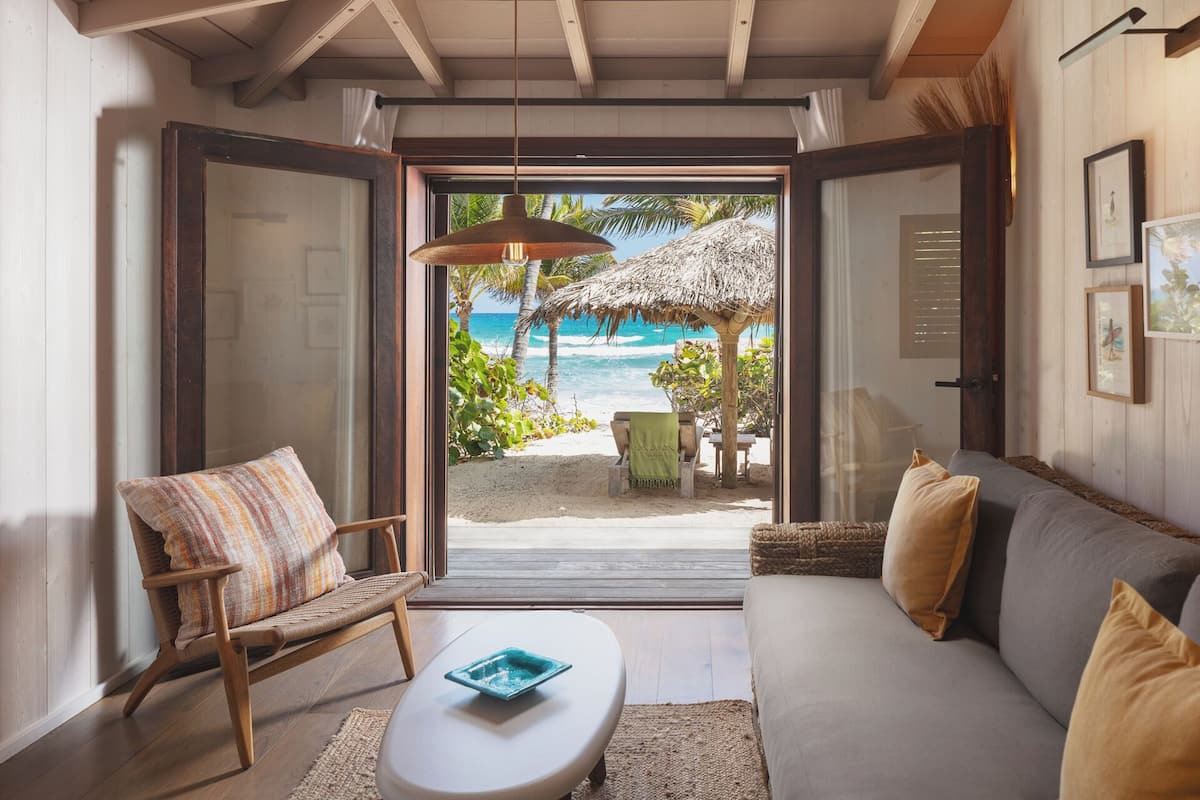 Une pièce avec vue sur la plage, une fenêtre à cadre en bois, une chaise en osier, un canapé et une petite table.