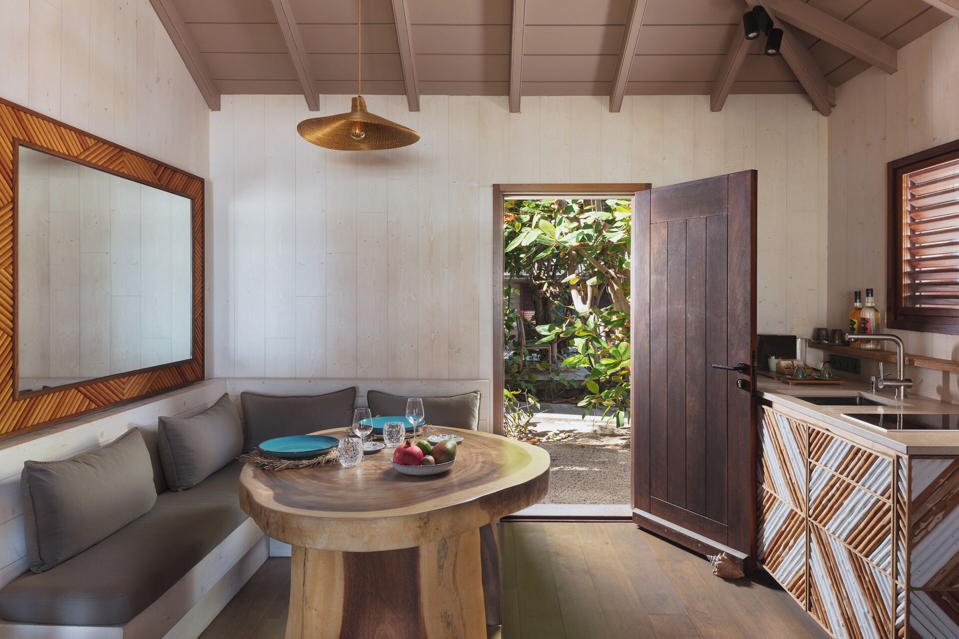 A cozy room with a wooden ceiling, a round wooden table with a bowl of fruit, a sofa, and a large mirror.