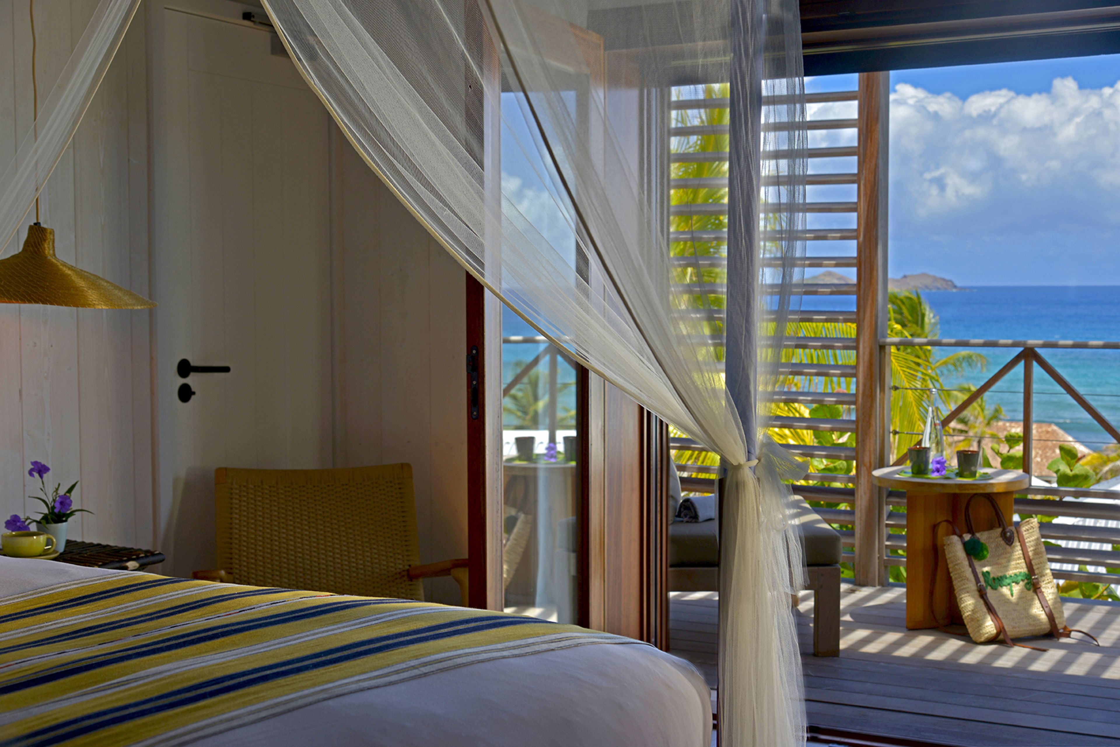 A room with a bed, a chair, a table, and a view of the ocean.