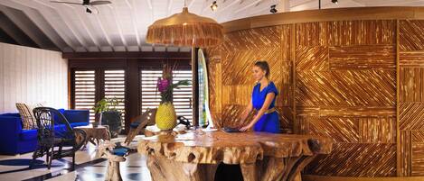 A lobby with a wooden reception desk, blue seating, and a ceiling fan.