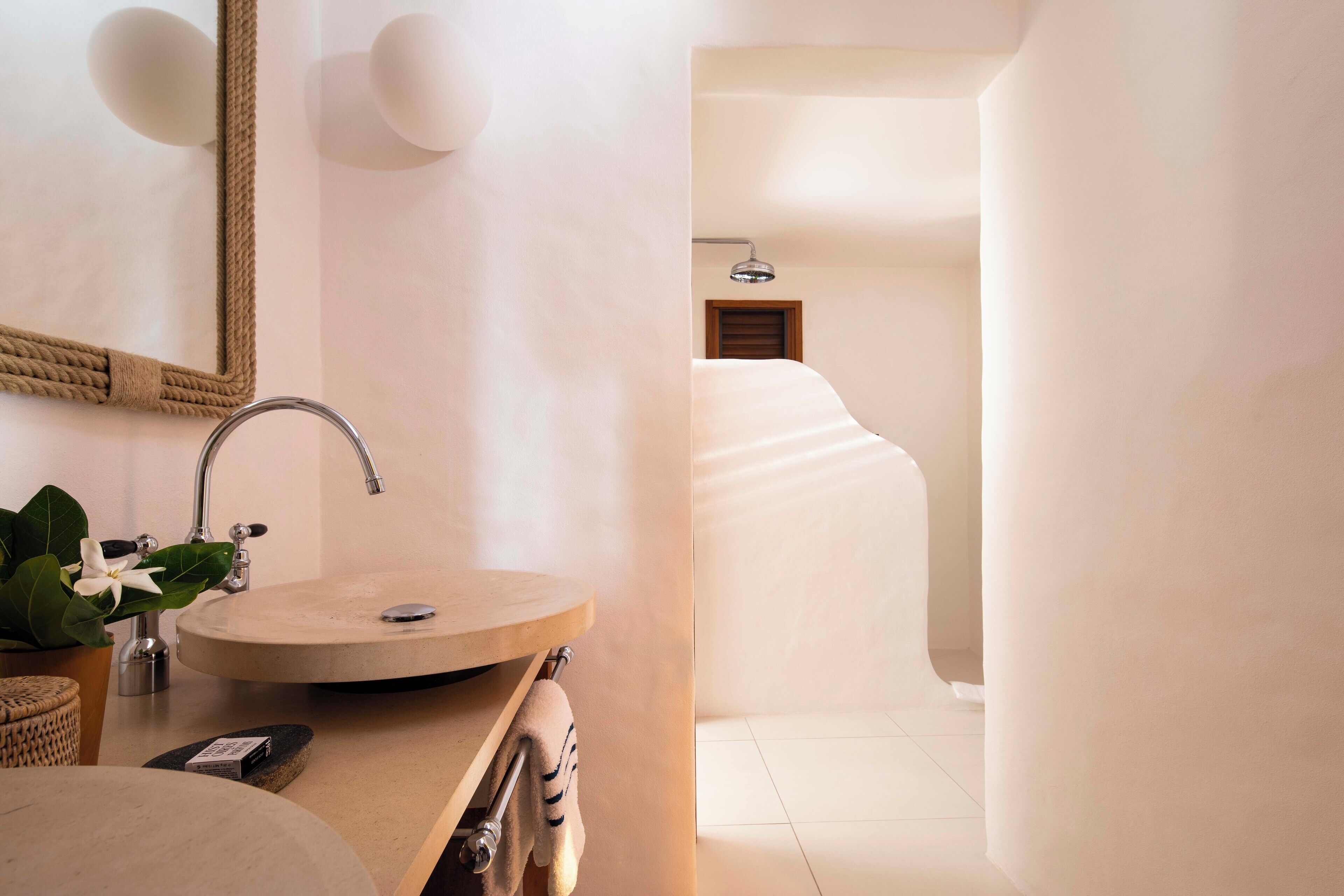 A modern bathroom with a round sink, a mirror with a rope frame, and a wooden towel rack.