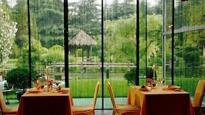 Un espace repas avec des tables préparées pour deux personnes, donnant sur un jardin luxuriant agrémenté d’un belvédère.