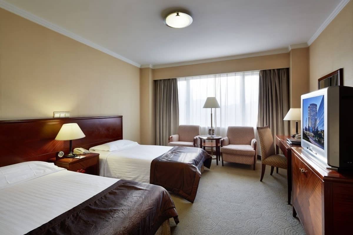 Une chambre d’hôtel avec deux lits, un bureau avec une télévision, une chaise et une lampe.