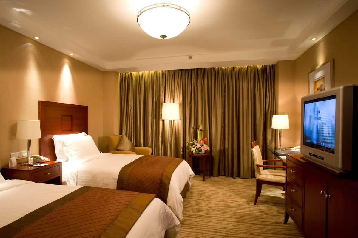 Une chambre d’hôtel avec deux lits, une télévision, un bureau avec une lampe et une chaise.