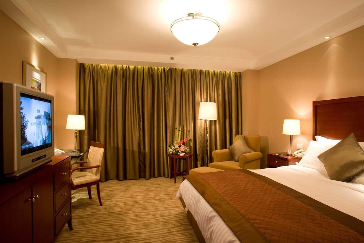 Une chambre d’hôtel comprenant un lit, deux chaises, un bureau avec une télévision et deux lampes.