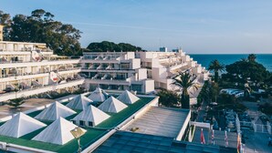 Ein Küstenhotel mit mehreren weißen Gebäuden, einem Dachgarten mit weißen Zelten und Blick auf das Meer.