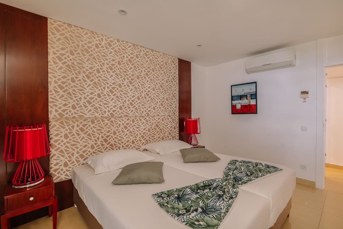 Habitación de hotel con cama, dos lámparas rojas, un papel tapiz estampado y un cuadro en la pared.