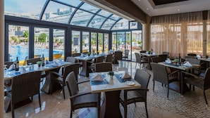 Ein Restaurant mit gedeckten Tischen, große Fenster mit Blick auf einen Pool und Resortbereich.