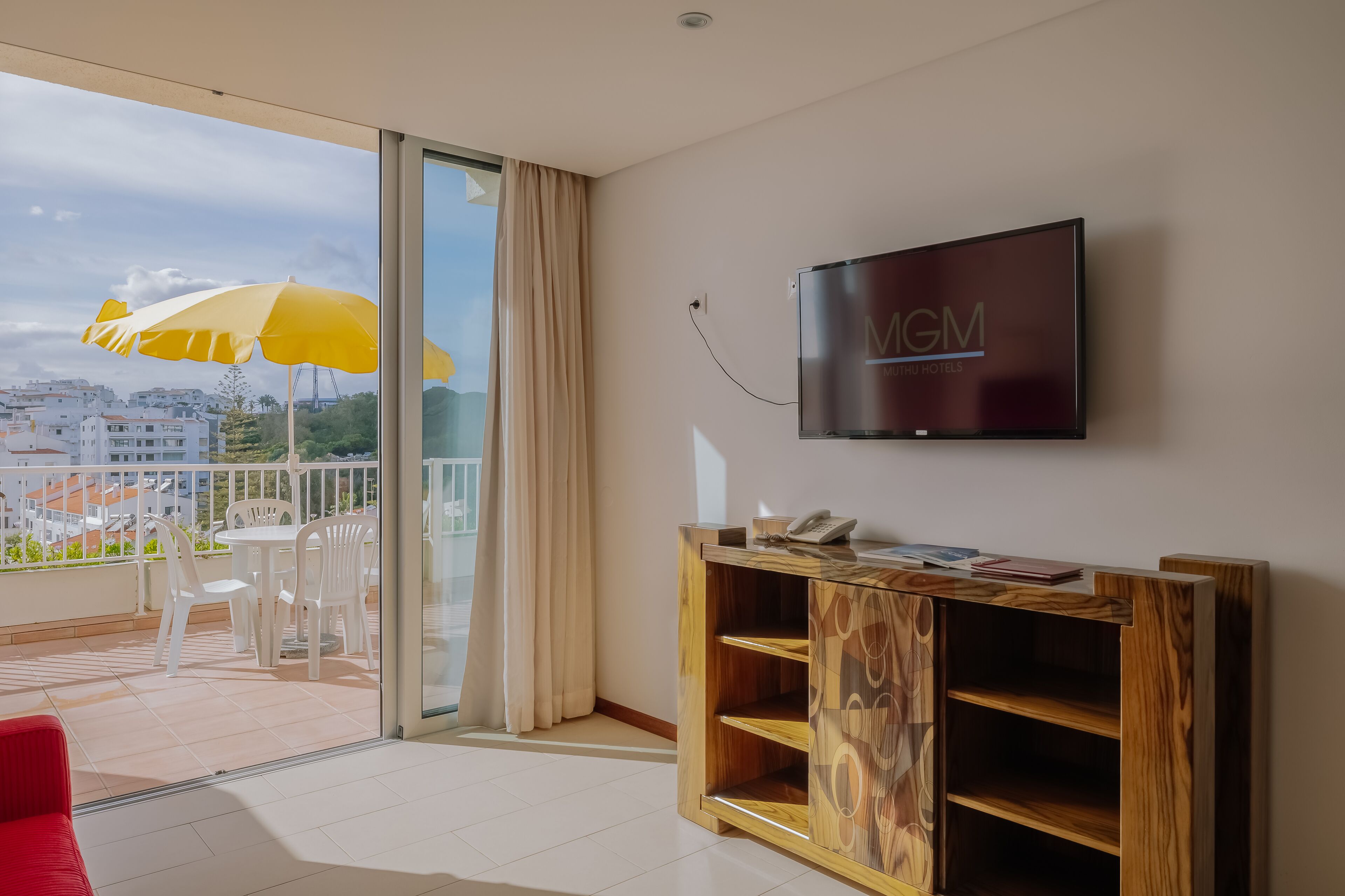 A modern hotel room with a balcony, a flat-screen TV, and a wooden cabinet.