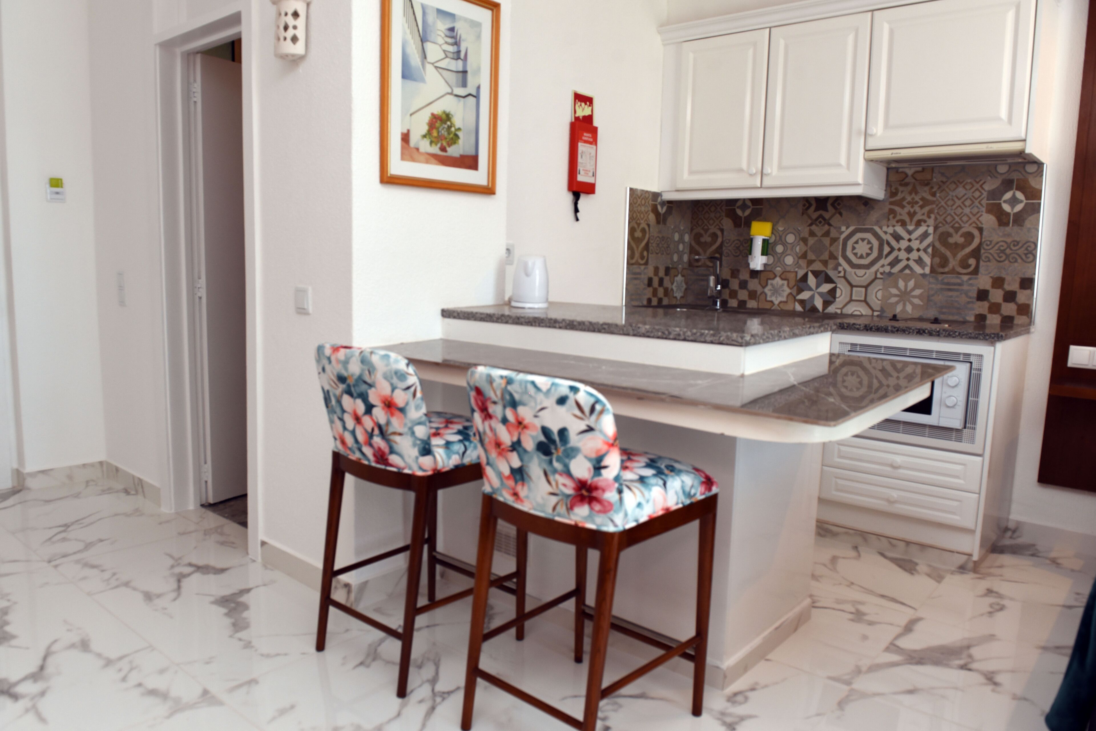 A kitchen with a marble floor, two bar stools, a coffee maker, and patterned backsplash.