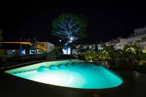 Relax by the illuminated pool surrounded by a unique tree sculpture and urban architecture.