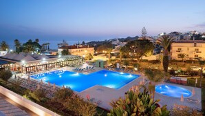 Ein großer Pool im Freien mit Liegestühlen und Sonnenschirmen, umgeben von Palmen und Gebäuden.
