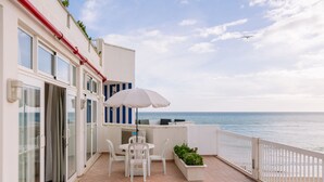 Ein Balkon mit Tisch und Stühlen, einem weißen Sonnenschirm und Blick aufs Meer.