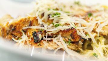 A close-up of a dish with grilled chicken, cheese, and herbs.