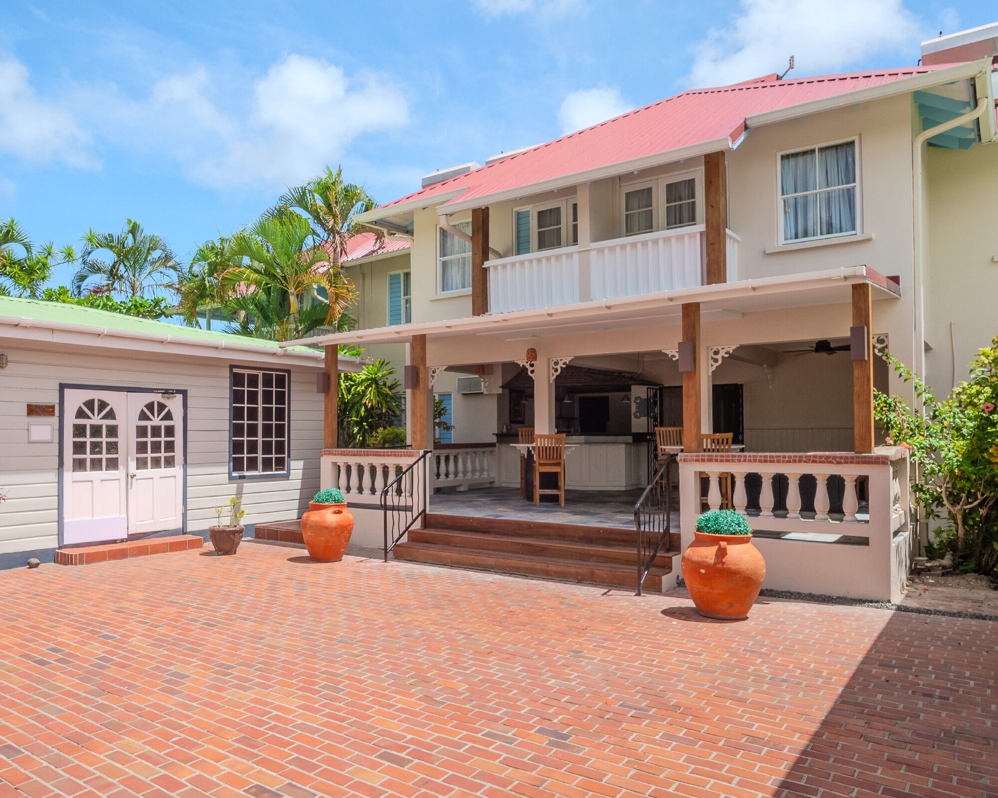 A two-story building with a covered porch, a brick patio, and potted plants.