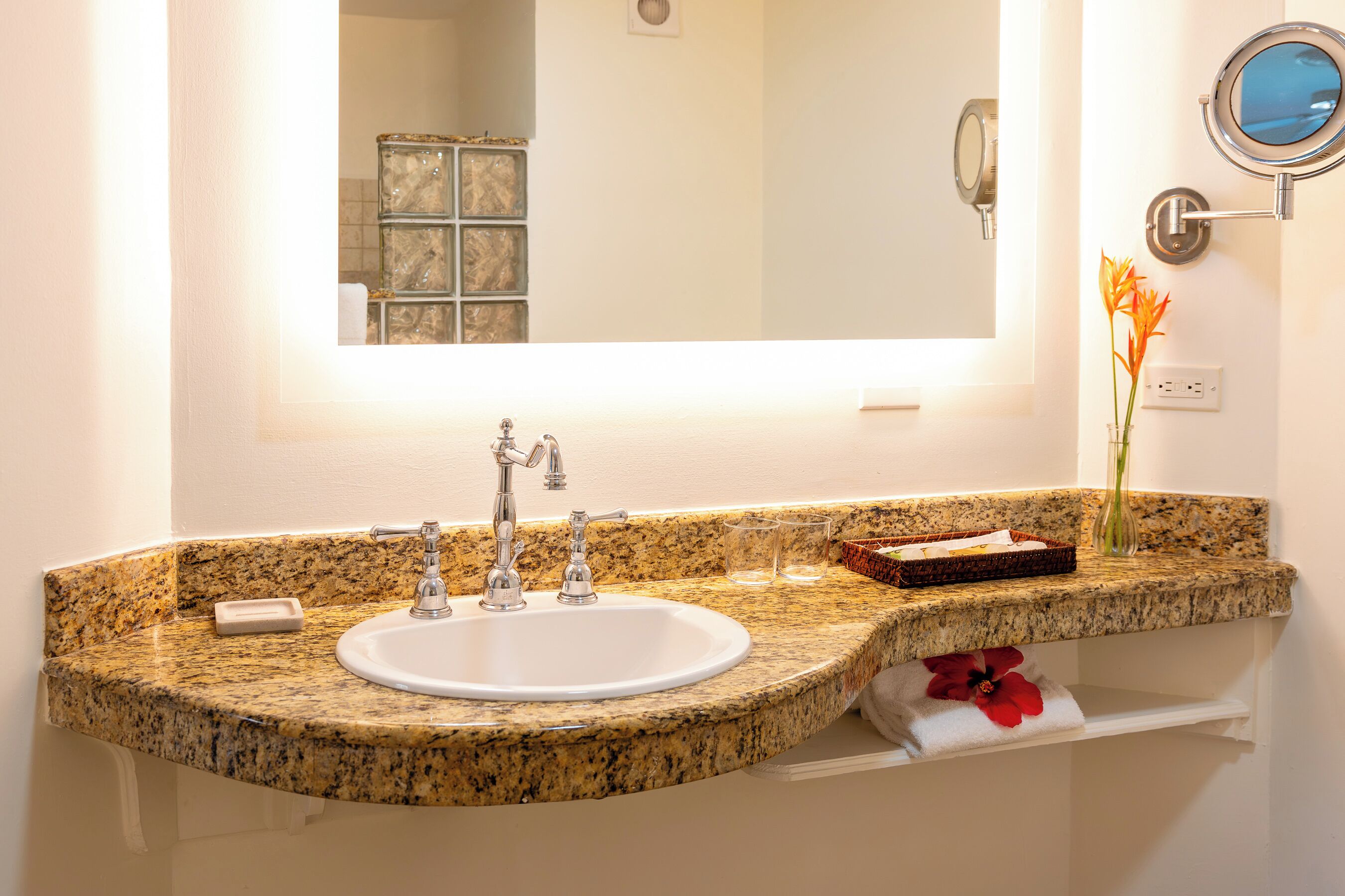 A bathroom with a granite countertop sink, a mirror, and a small vase with flowers.