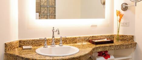 A bathroom with a granite countertop sink, a mirror, and a small vase with flowers.