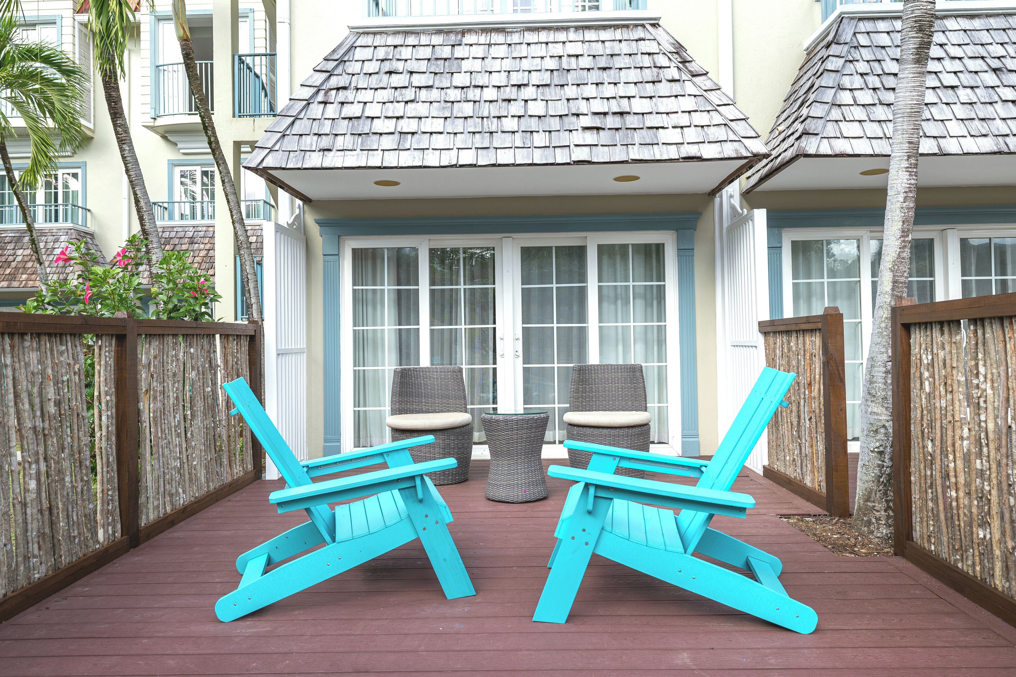 A deck with two turquoise Adirondack chairs and a wicker table.