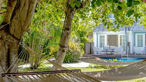 Una hamaca bajo un árbol, una piscina y una casa con mobiliario exterior.