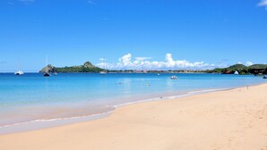 Una playa con agua azul cristalina, una orilla de arena y una pequeña isla al fondo.