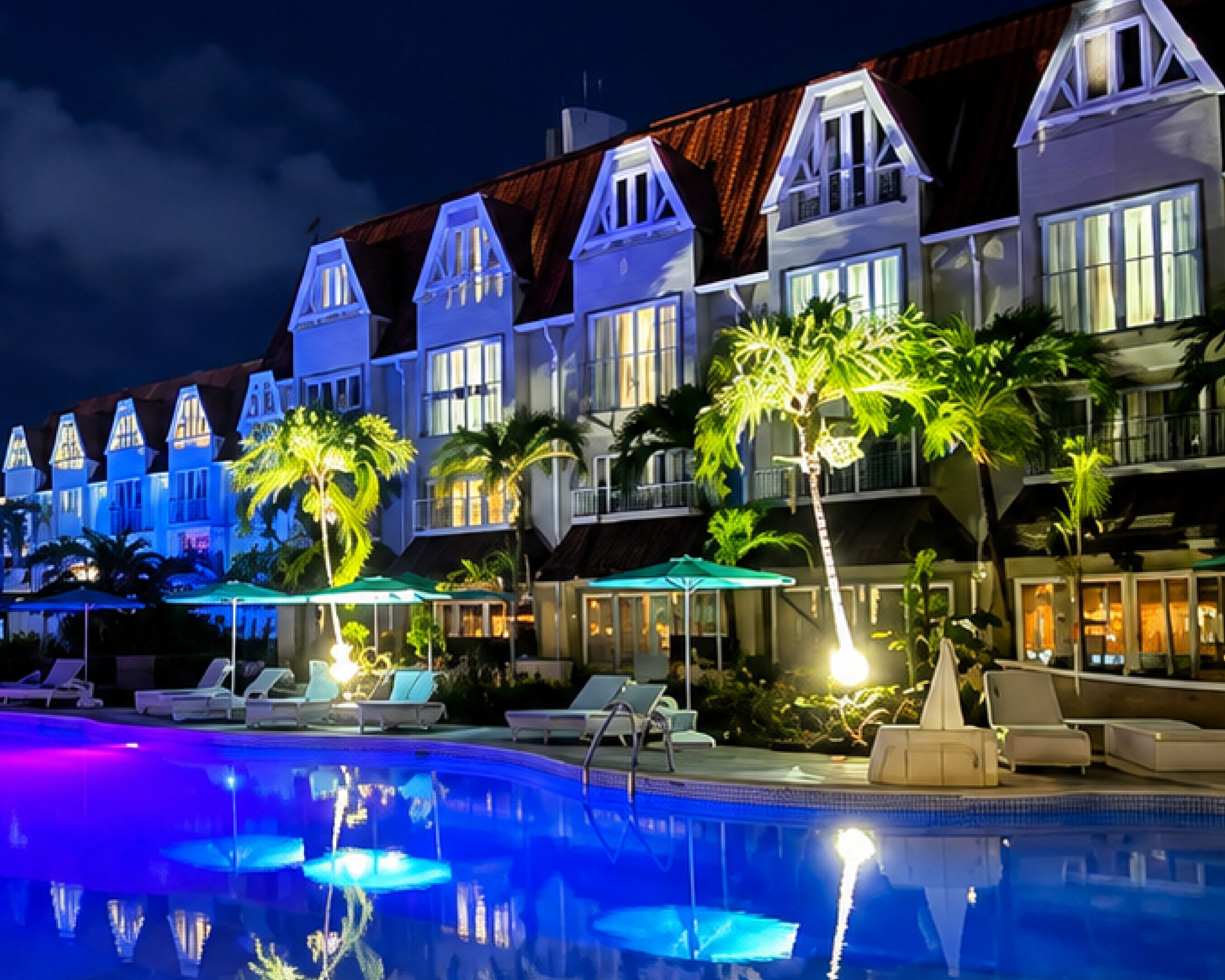 A hotel with multiple-story buildings, a swimming pool, and palm trees.