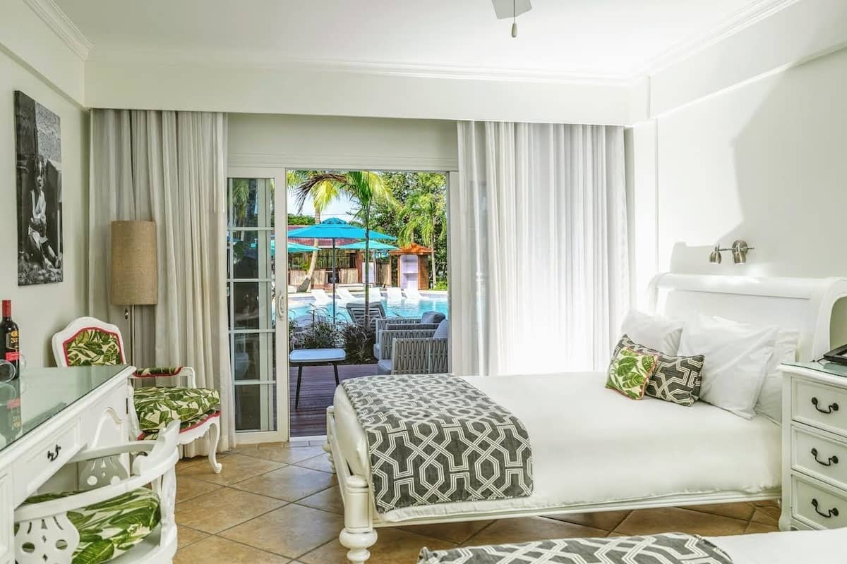 Habitación de hotel con cama, escritorio, silla y vista al área de piscina exterior.