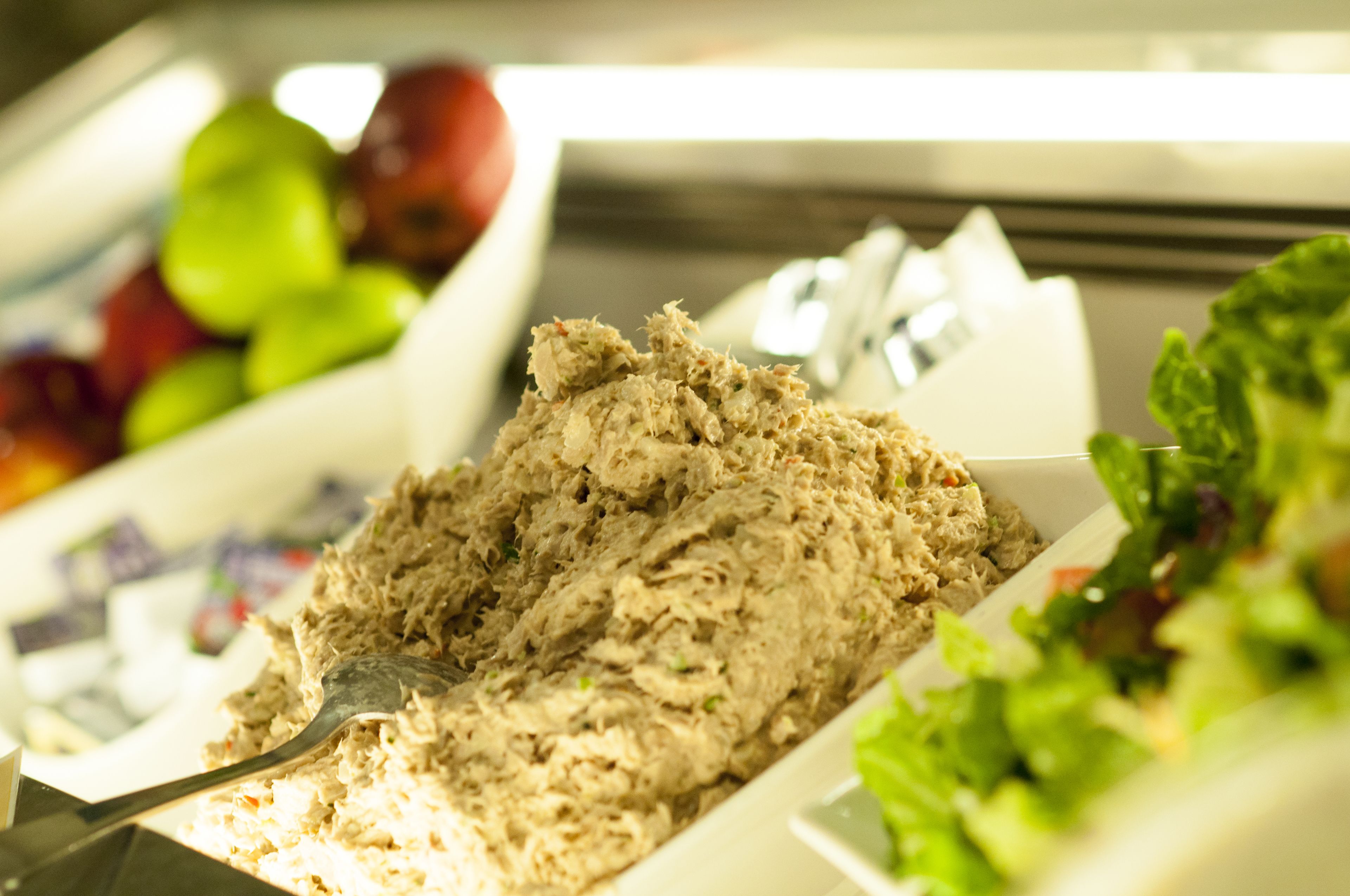 A buffet with a variety of food options including a dish with shredded meat, fresh fruits, and a salad.