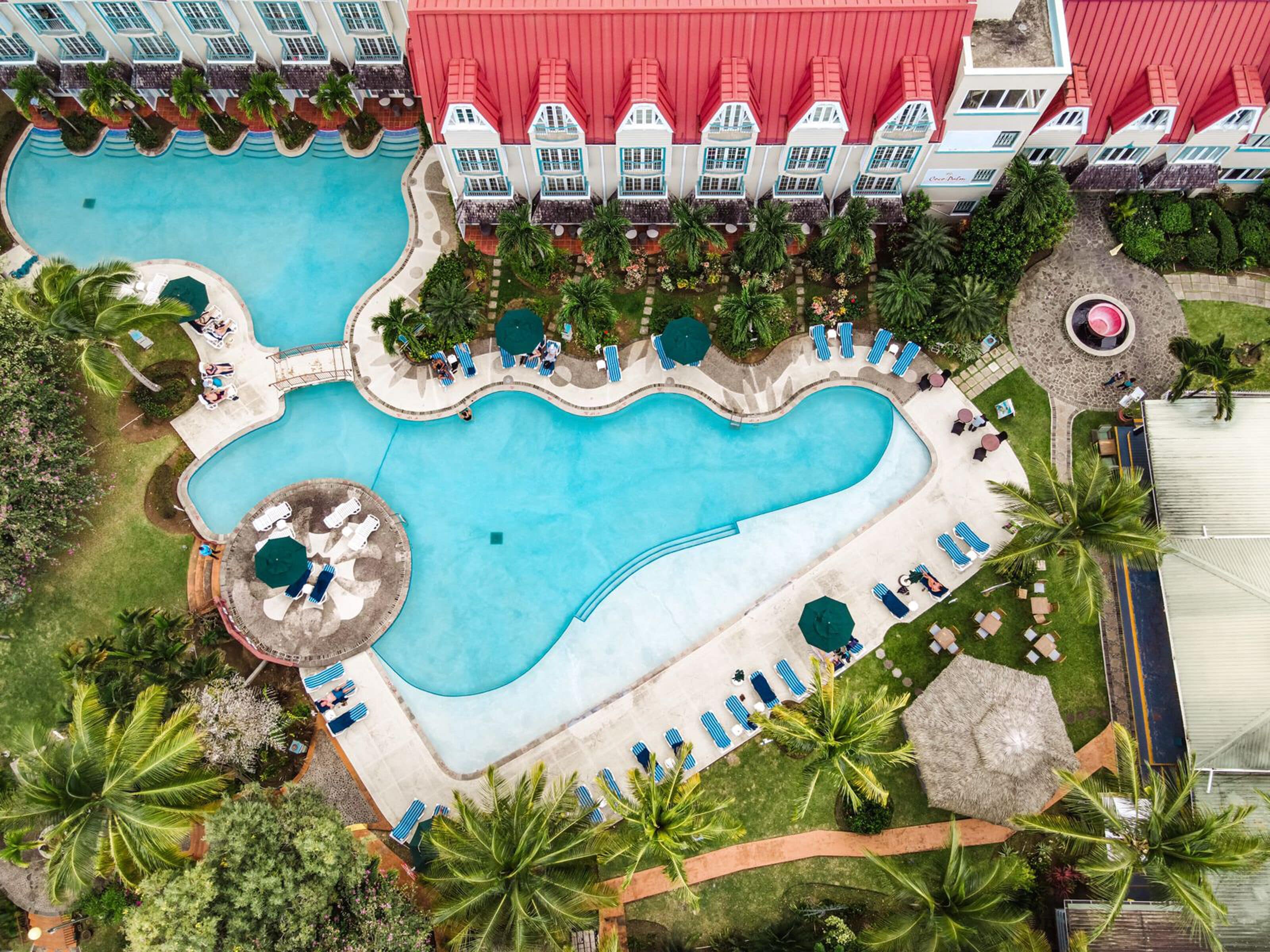 Una gran piscina con varias terrazas, rodeada de palmeras y tumbonas.